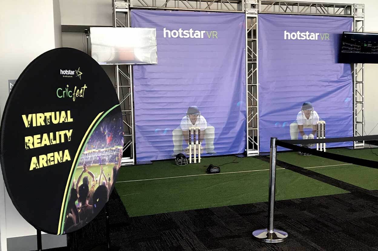 Two purple backdrops with wicketkeepers printed on them behind astroturf mats with cricket wickets.